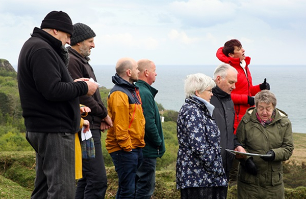 Members of the community and Flodigarry Township Trust look on as local MSP Kate Forbes cuts the first turf at the ceremony .
